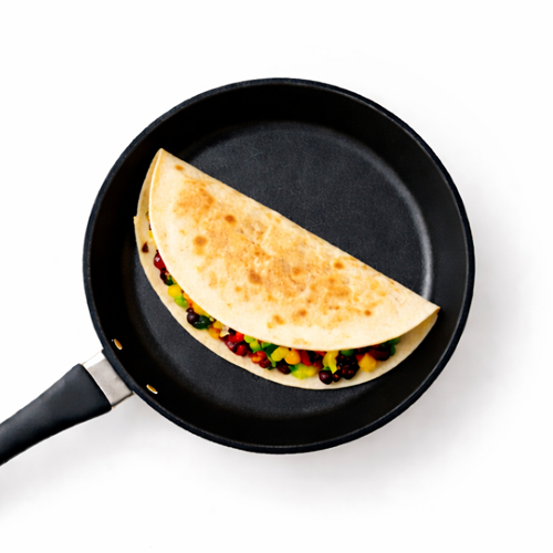 Quesadilla with colorful vegetables cooking in pan.