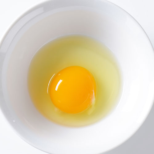 Egg yolk and white in a white bowl