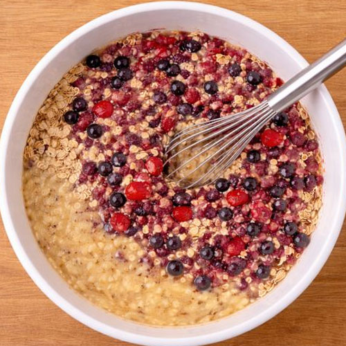 Whisk mixing oats with berries in white bowl